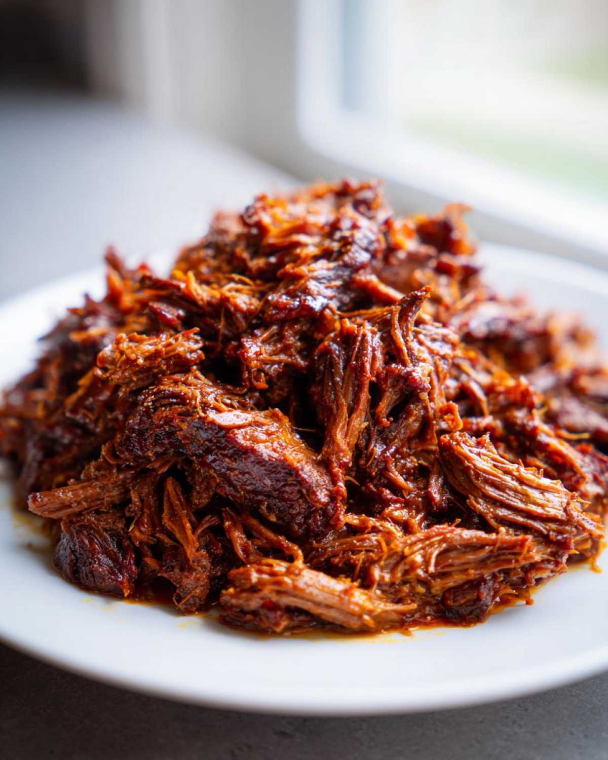 Close-up of richly seasoned, shredded Instant Pot Beef Barbacoa piled high on a white plate.