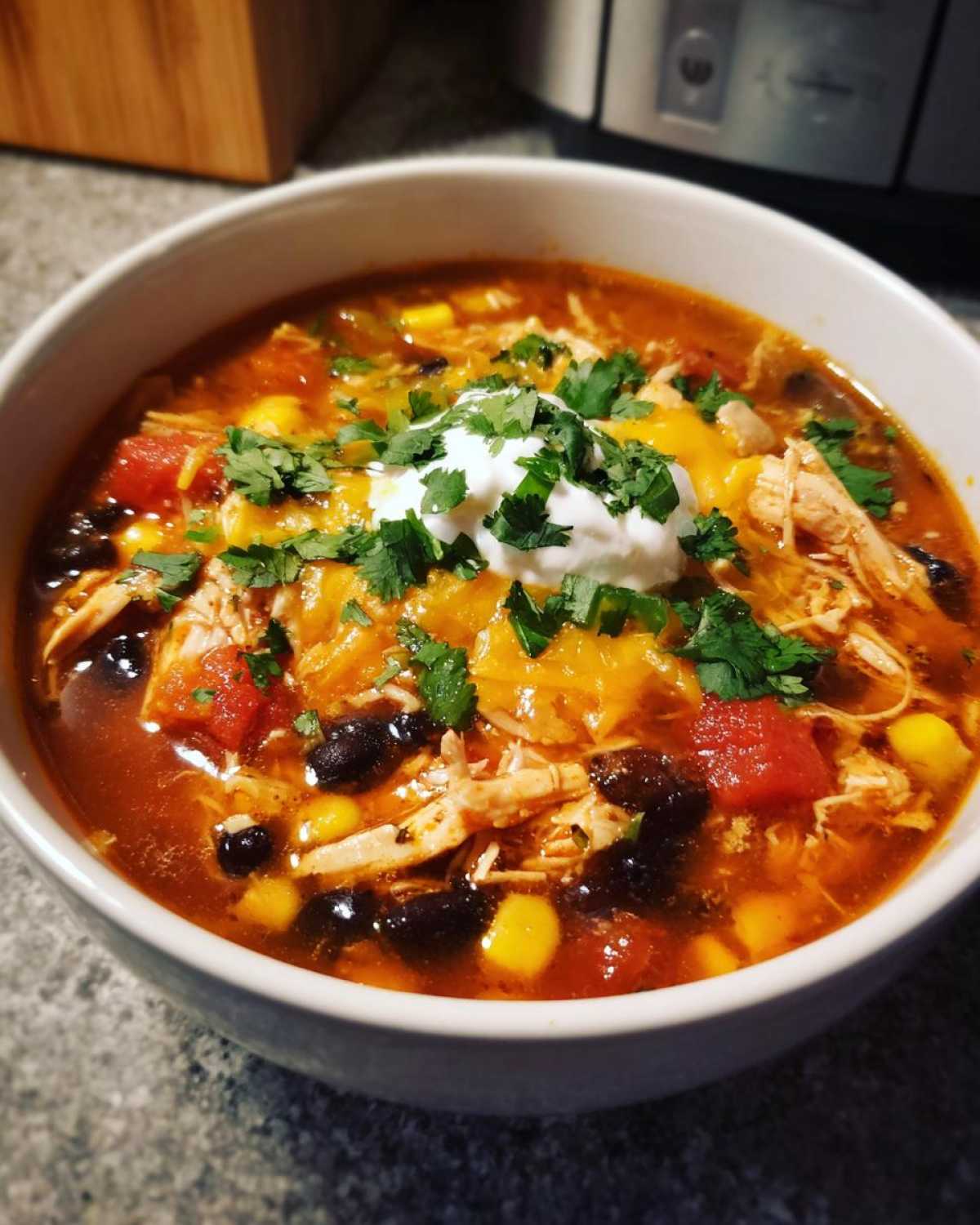 A close-up of a bowl of Instant Pot Chicken Tortilla Soup with shredded chicken, black beans, corn, cheese, sour cream, and cilantro.