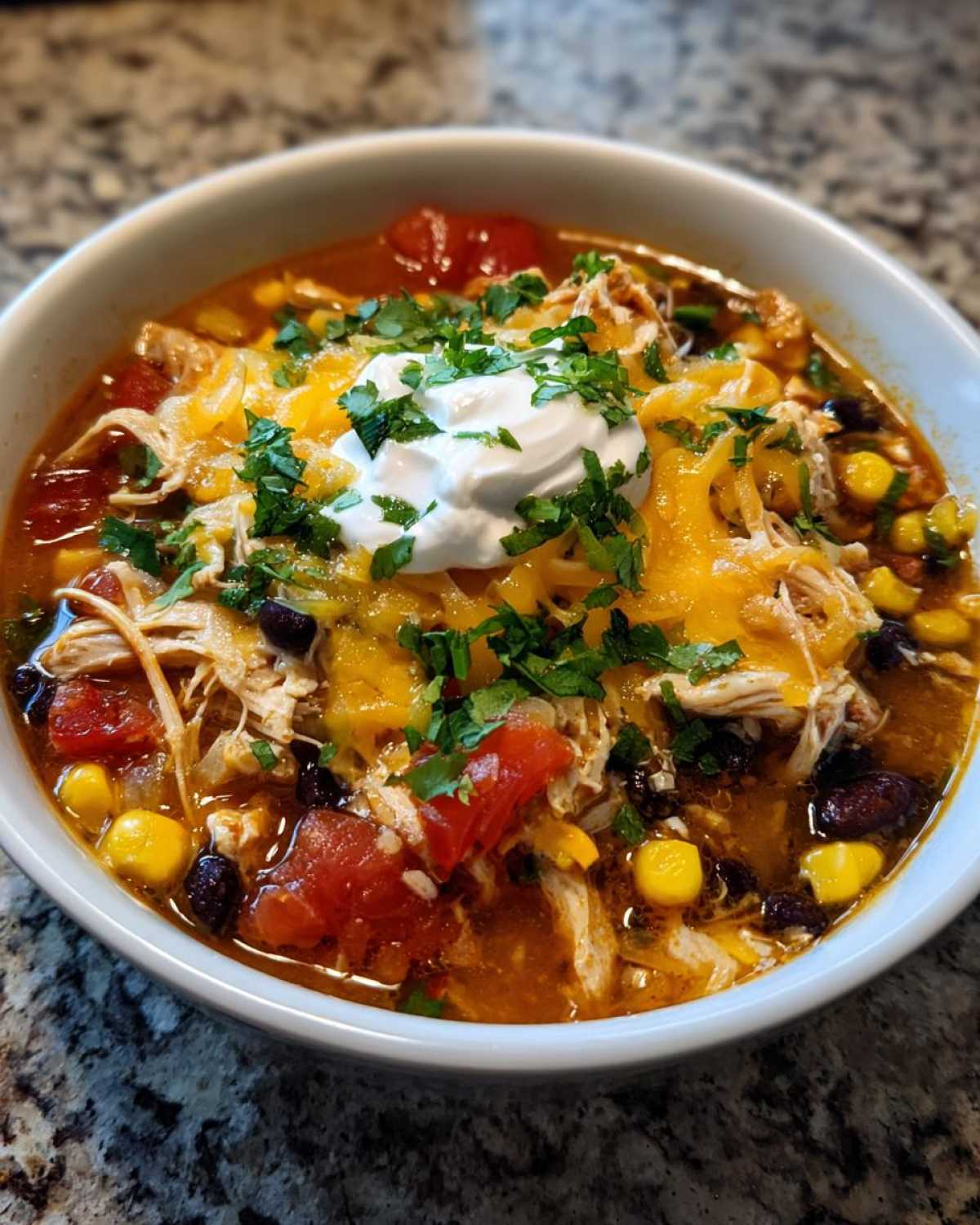 Close-up of a bowl of Instant Pot Chicken Tortilla Soup topped with shredded cheese, sour cream, and cilantro.