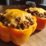 Two halves of bright orange Keto Taco Stuffed Peppers filled with seasoned ground meat and topped with melted cheddar cheese.