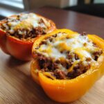 Two halves of Keto Taco Stuffed Peppers, one yellow and one orange, filled with seasoned meat and topped with melted cheese.
