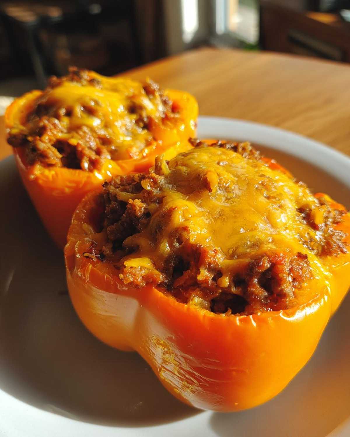Two bright orange bell peppers stuffed with seasoned taco meat and topped with melted cheddar cheese, ready to eat as Keto Taco Stuffed Peppers.