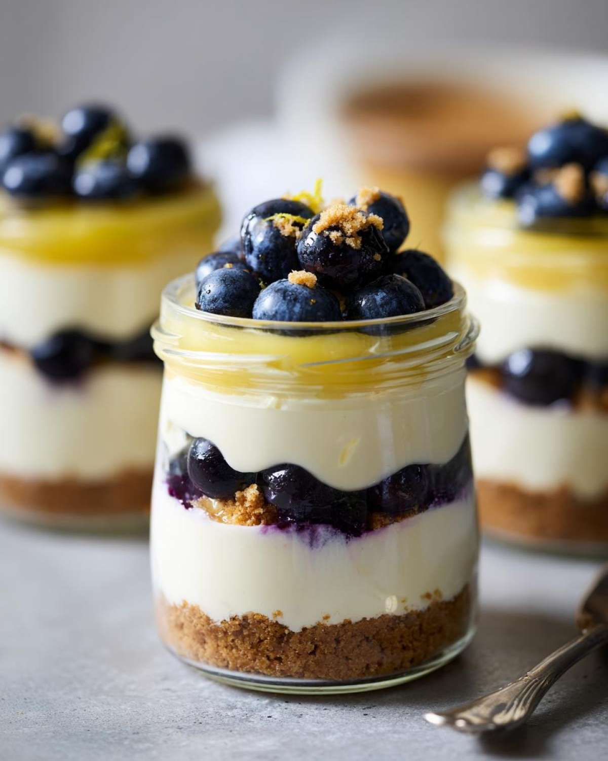 Close-up of a layered Lemon Blueberry Cheesecake Jar dessert topped with fresh blueberries and lemon zest.