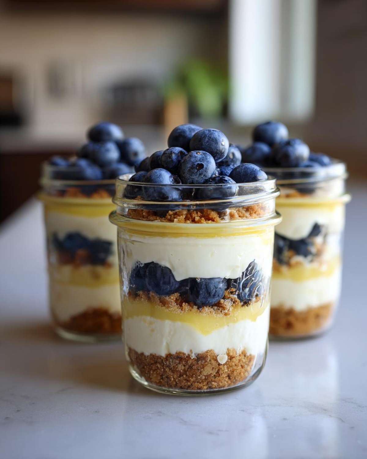 Three layered Lemon Blueberry Cheesecake Jars topped generously with fresh blueberries.