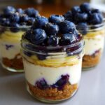Three individual Lemon Blueberry Cheesecake Jars featuring graham cracker crust, creamy filling, and a generous topping of fresh blueberries.