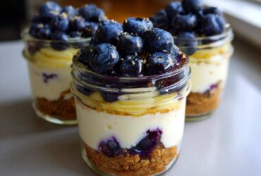 Three individual Lemon Blueberry Cheesecake Jars featuring graham cracker crust, creamy filling, and a generous topping of fresh blueberries.