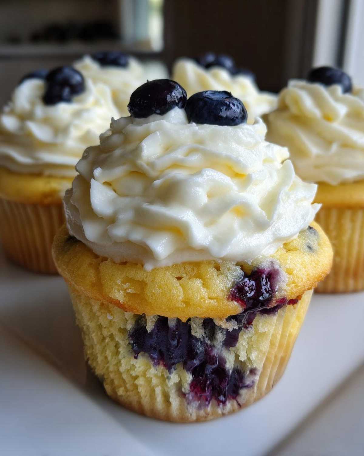 Close-up of a Lemon Blueberry Cupcake topped with swirls of cream cheese frosting and fresh blueberries.