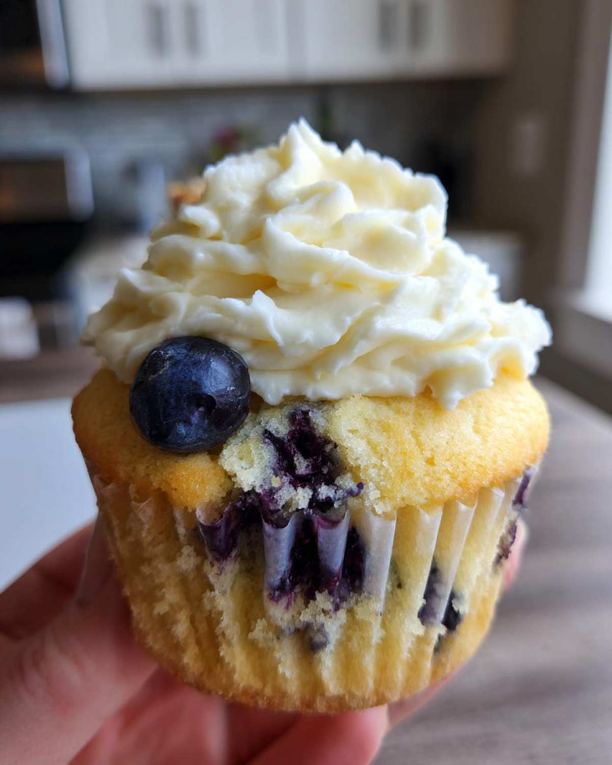 A close-up of a single Lemon Blueberry Cupcake with Cream Cheese Frosting, topped with one fresh blueberry.