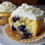 Close-up of a Lemon Blueberry Cupcakes with Cream Cheese Frosting cut in half, showing moist cake and blueberries.