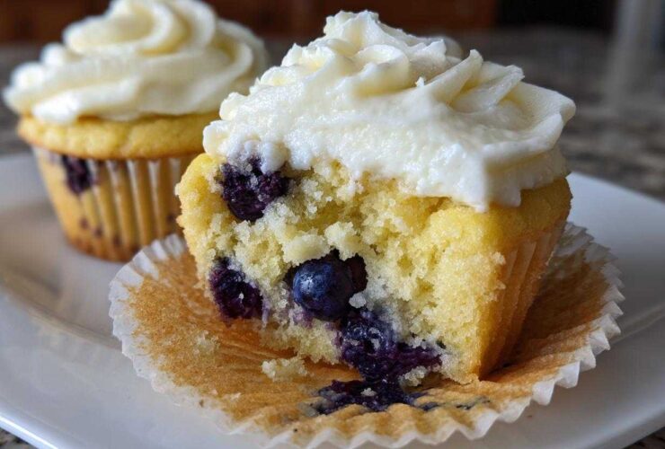 Close-up of a Lemon Blueberry Cupcakes with Cream Cheese Frosting cut in half, showing moist cake and blueberries.