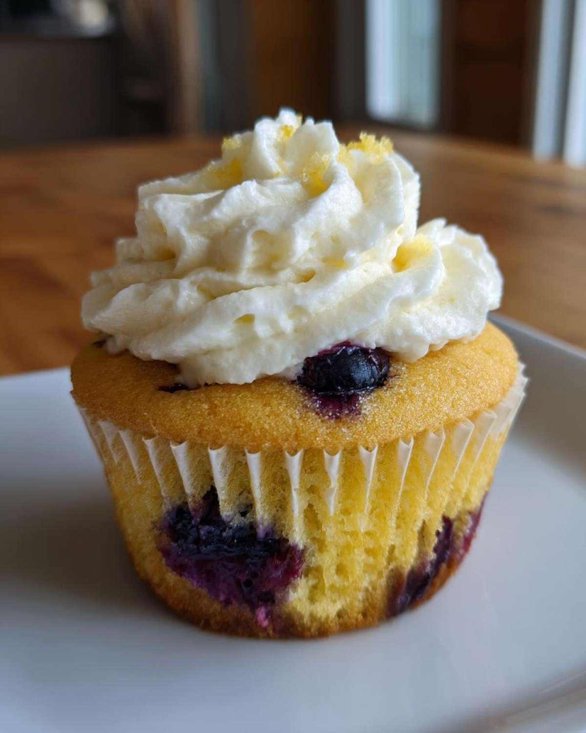 A single, bright yellow Lemon Blueberry Cupcake with Cream Cheese Frosting topped with lemon zest.