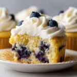 Close-up of a Lemon Blueberry Cupcakes with Cream Cheese Frosting, showing the moist crumb and burst blueberries inside.