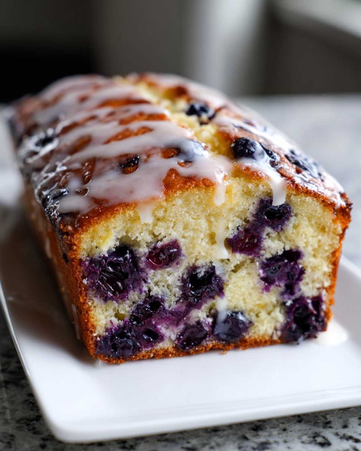 A moist Lemon Blueberry Yogurt Loaf, studded with dark blueberries and topped with a white lemon glaze.