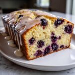 A close-up of a freshly baked Lemon Blueberry Yogurt Loaf drizzled with a thick white glaze.