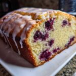 A close-up of a moist Lemon Blueberry Yogurt Loaf topped with a sweet white glaze.