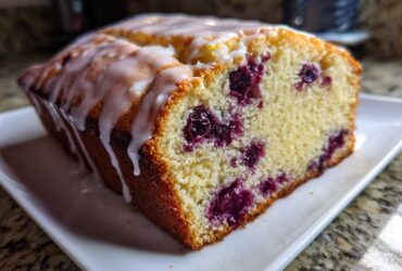 A close-up of a moist Lemon Blueberry Yogurt Loaf topped with a sweet white glaze.