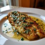 Close-up of a perfectly cooked Lemon Garlic Butter Tilapia fillet swimming in sauce and topped with fresh parsley.