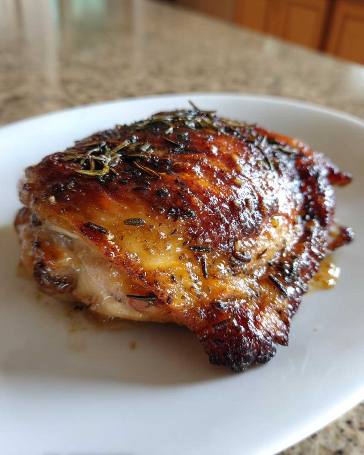 Close-up of a juicy, roasted Lemon Garlic Chicken Thigh with deeply browned, crispy skin topped with herbs.