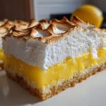 A close-up view of a thick slice of Lemon Meringue Pie Bars, showing the crust, bright yellow filling, and toasted meringue.