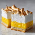 Close-up of two squares of Lemon Meringue Pie Bars showing crust, bright yellow filling, and torched meringue.