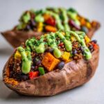 Close-up of a Loaded Veggie Stuffed Sweet Potato topped with quinoa, beans, vegetables, and a bright green sauce.
