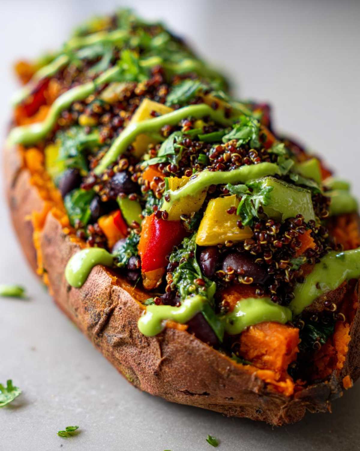 Close-up of Loaded Veggie Stuffed Sweet Potatoes topped with quinoa, colorful vegetables, and a bright green drizzle.