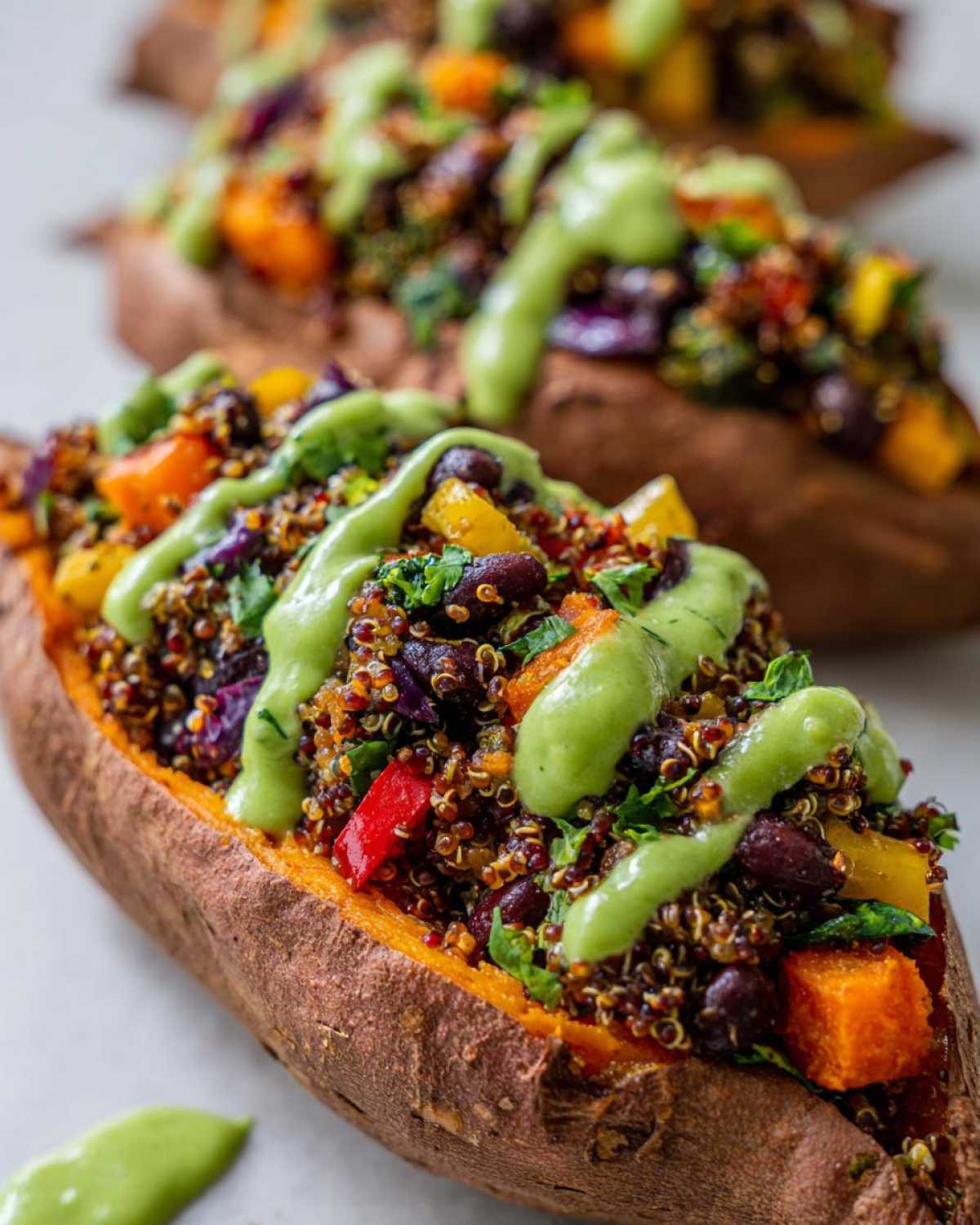 Close-up of Loaded Veggie Stuffed Sweet Potatoes topped with quinoa, beans, vegetables, and a bright green sauce.