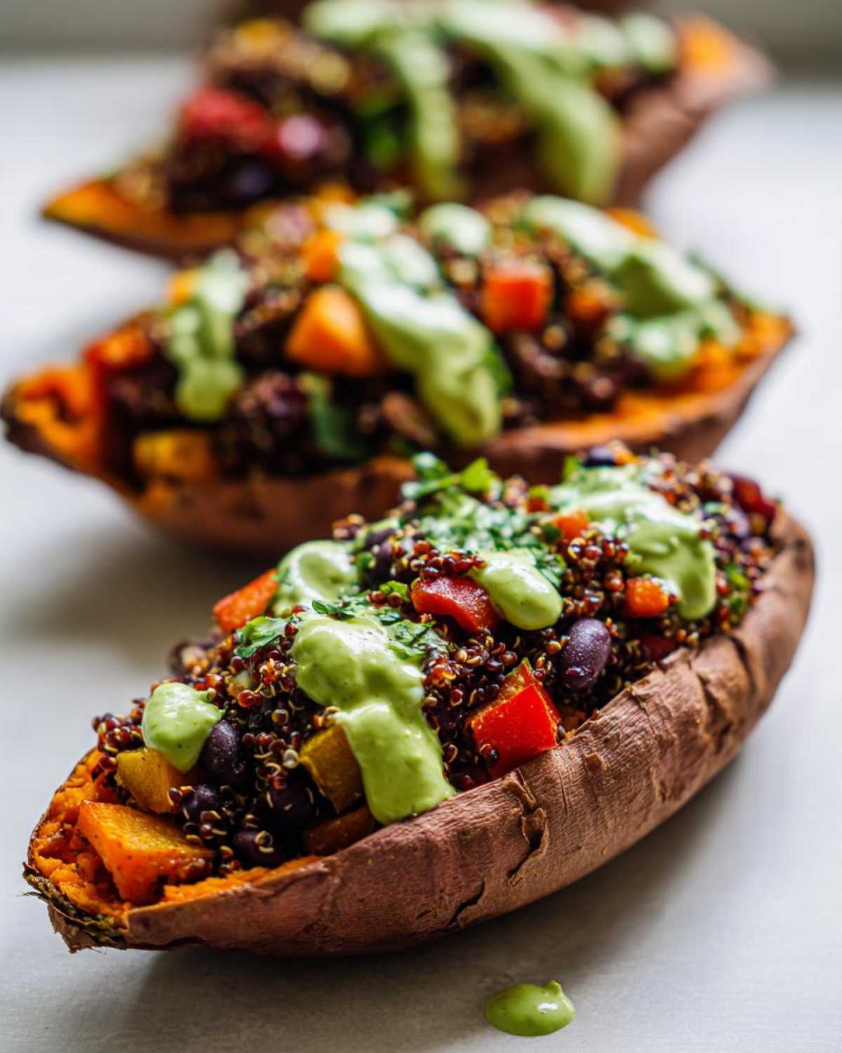 Close-up of Loaded Veggie Stuffed Sweet Potatoes filled with quinoa, beans, peppers, and drizzled with green sauce.
