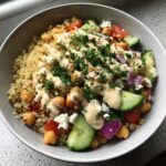 A vibrant Mediterranean Quinoa Bowl topped with chickpeas, cucumber, feta, and drizzled with lemon tahini sauce.
