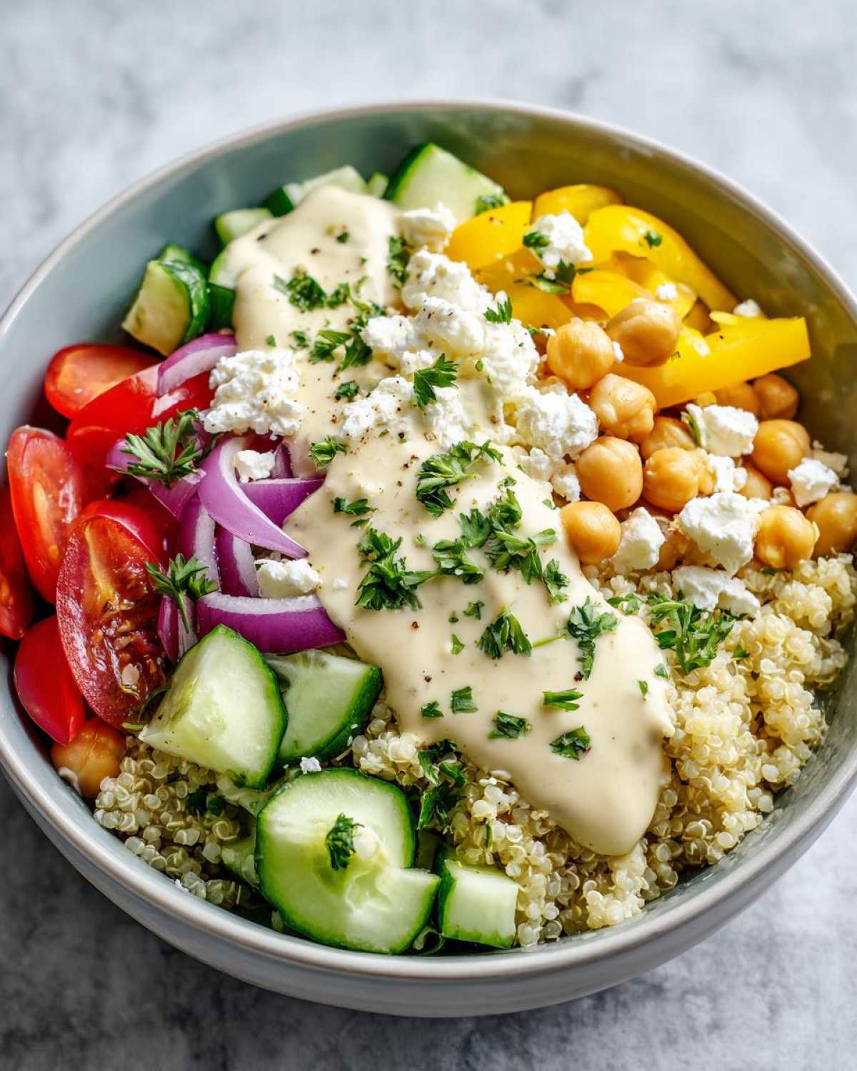 Close-up of a Mediterranean Quinoa Bowl with lemon tahini sauce, feta, chickpeas, cucumbers, and tomatoes.
