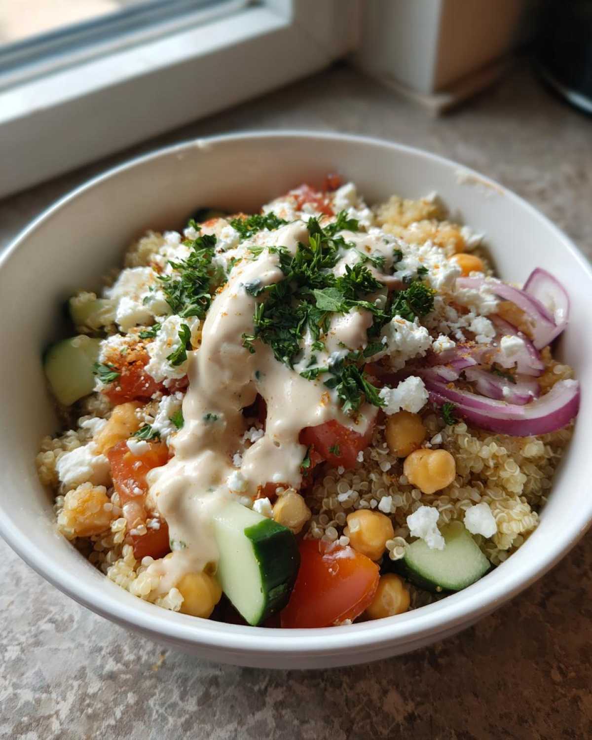 Close-up of a Mediterranean Quinoa Bowl topped with feta, chickpeas, cucumber, and lemon tahini sauce.