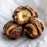 Close-up of No-Bake Chocolate Covered Banana Bites, one cut open revealing banana center, drizzled with peanut butter.
