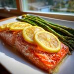 A close-up of a cooked salmon fillet topped with lemon slices, next to roasted asparagus, prepared for One-Pan Lemon Garlic Salmon with Asparagus.