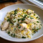A white bowl filled with creamy One-Pot Chicken and Rice with Lemon and Herbs, topped with fresh parsley and lemon zest.