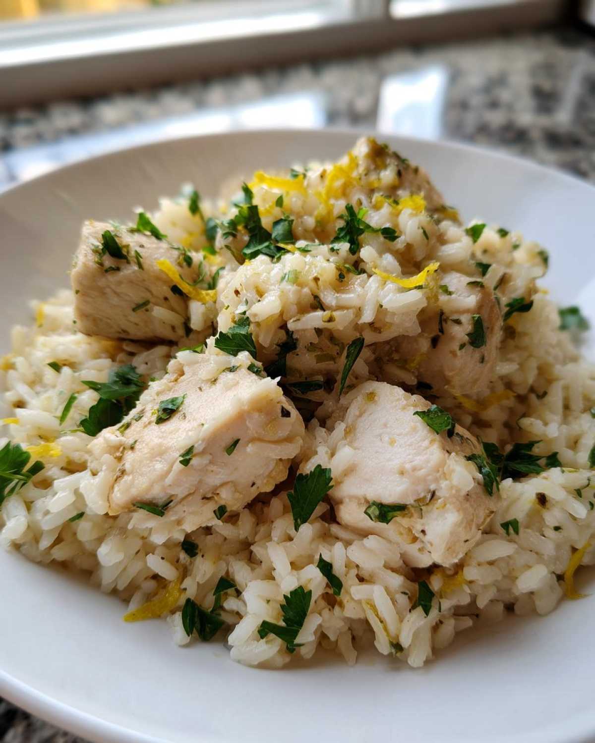 Close-up of cooked chicken pieces served over fluffy rice, garnished with fresh parsley and lemon zest for One-Pot Chicken and Rice with Lemon and Herbs.