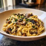 A close-up of a white bowl filled with One-Pot Creamy Mushroom Orzo, topped with sautéed mushrooms and fresh herbs.