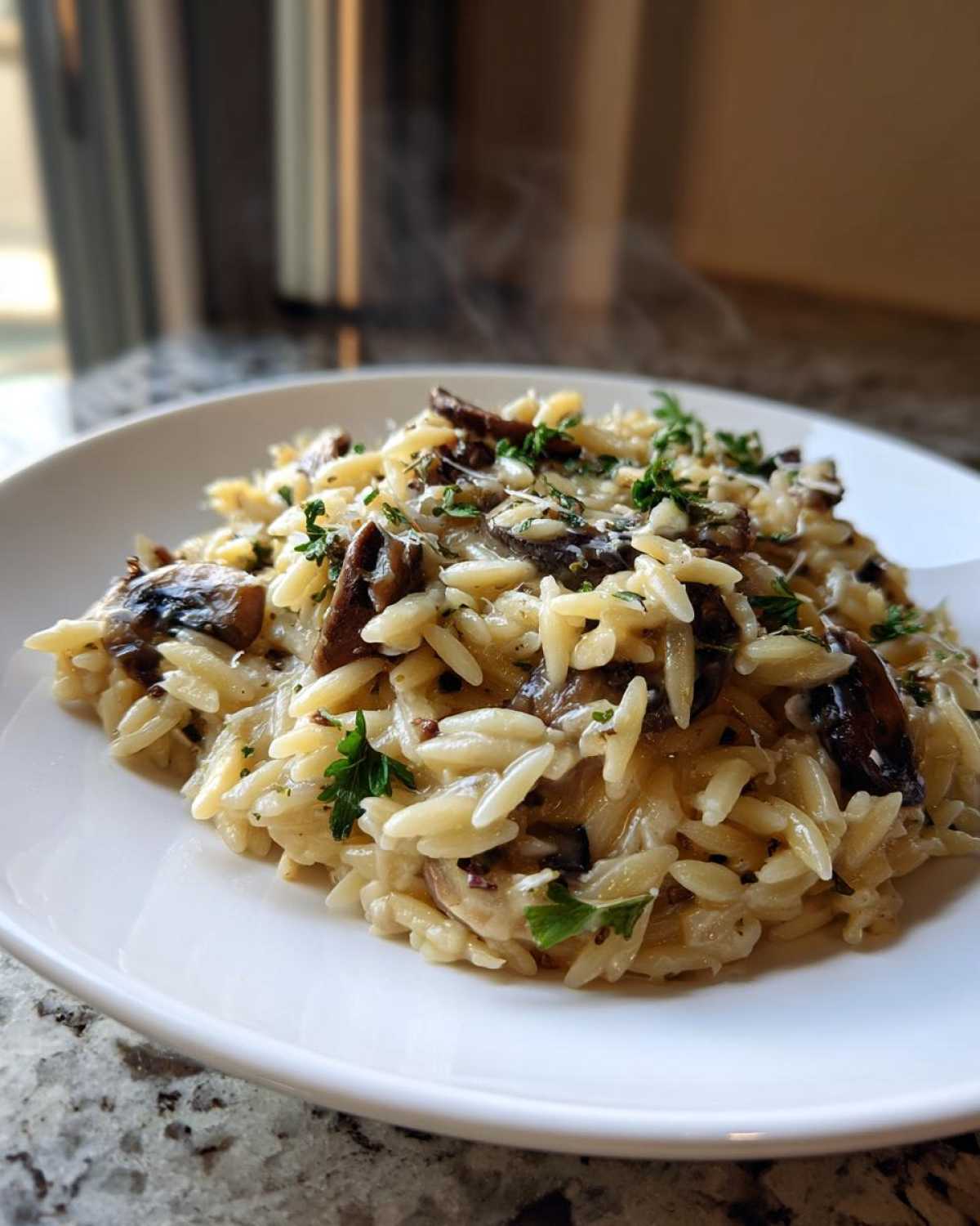 Close-up of steaming One-Pot Creamy Mushroom Orzo topped with mushrooms and fresh parsley on a white plate.