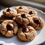 A pile of freshly baked Peanut Butter Blossom Cookies rolled in sugar with a chocolate kiss pressed into the center.
