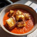 A bowl of vibrant Roasted Tomato Basil Soup topped with golden Grilled Cheese Croutons and grated Parmesan.
