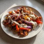 Plate of Sheet Pan Chicken Shawarma topped with red onions and creamy garlic yogurt sauce.