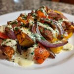 Close-up of Sheet Pan Chicken Shawarma pieces and roasted vegetables drizzled with garlic yogurt sauce.