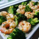 Close-up of cooked shrimp and bright green broccoli florets seasoned with garlic butter on a sheet pan.