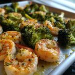 Close-up of cooked shrimp and broccoli florets seasoned with garlic butter on a sheet pan.
