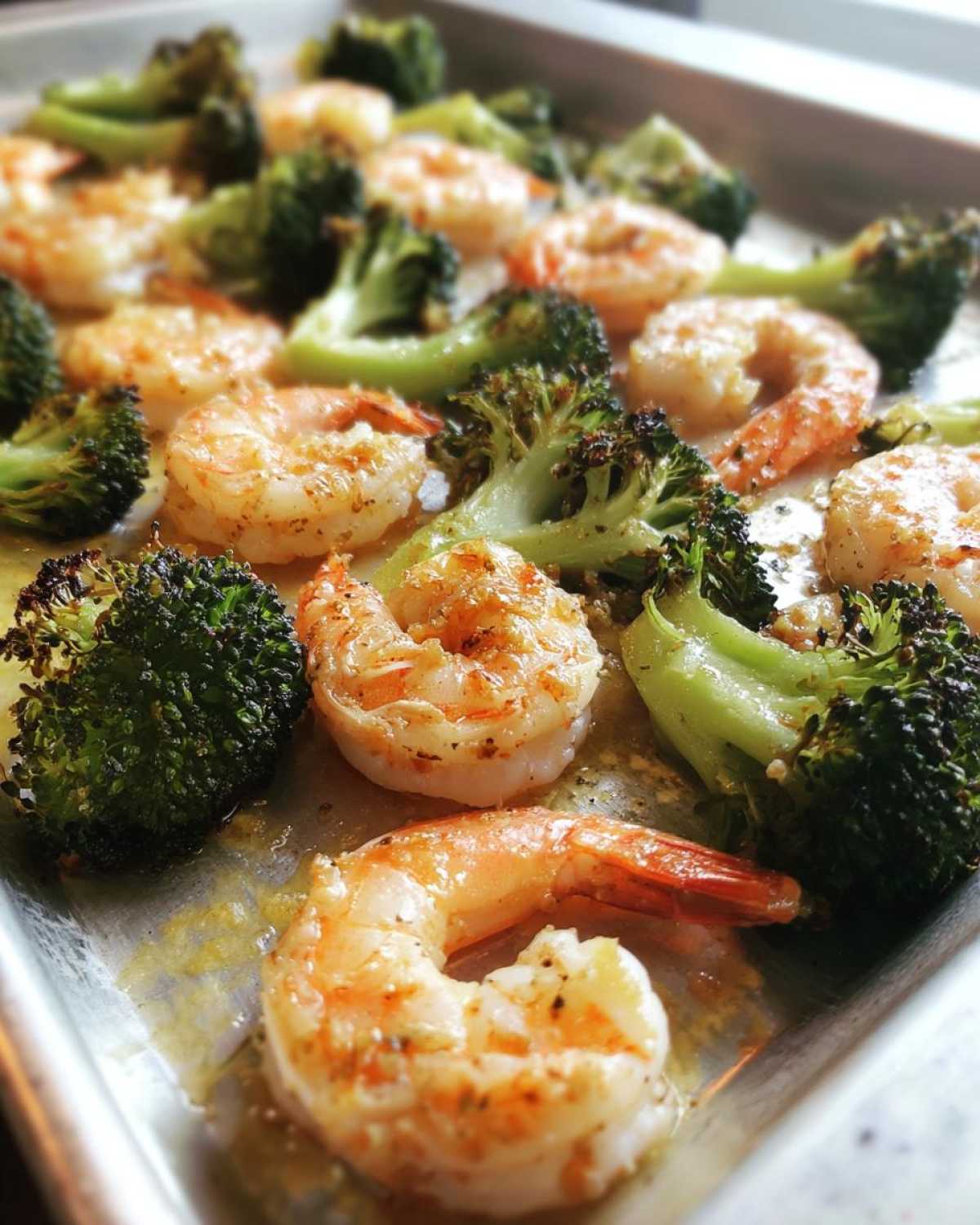 Close-up of cooked Sheet Pan Garlic Butter Shrimp and Broccoli glistening with butter on a metal baking sheet.