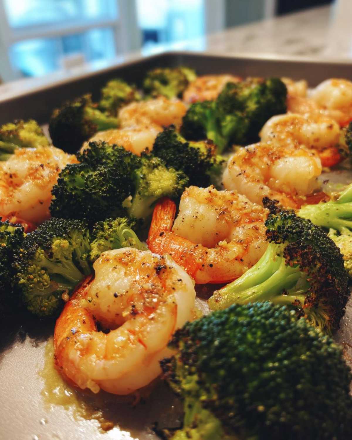 Close-up of cooked shrimp and roasted broccoli florets on a sheet pan, coated in garlic butter.