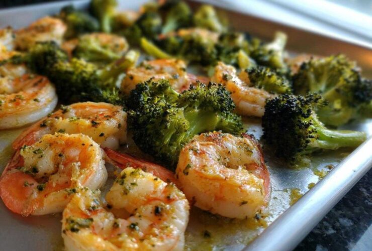 Close-up of cooked shrimp and broccoli florets seasoned with garlic butter on a sheet pan.