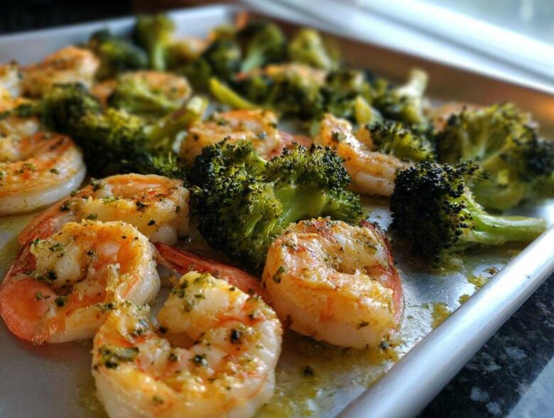 Close-up of cooked shrimp and broccoli florets seasoned with garlic butter on a sheet pan.