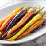 Close-up of glistening, roasted Sheet Pan Roasted Rainbow Carrots with Honey on a white platter.