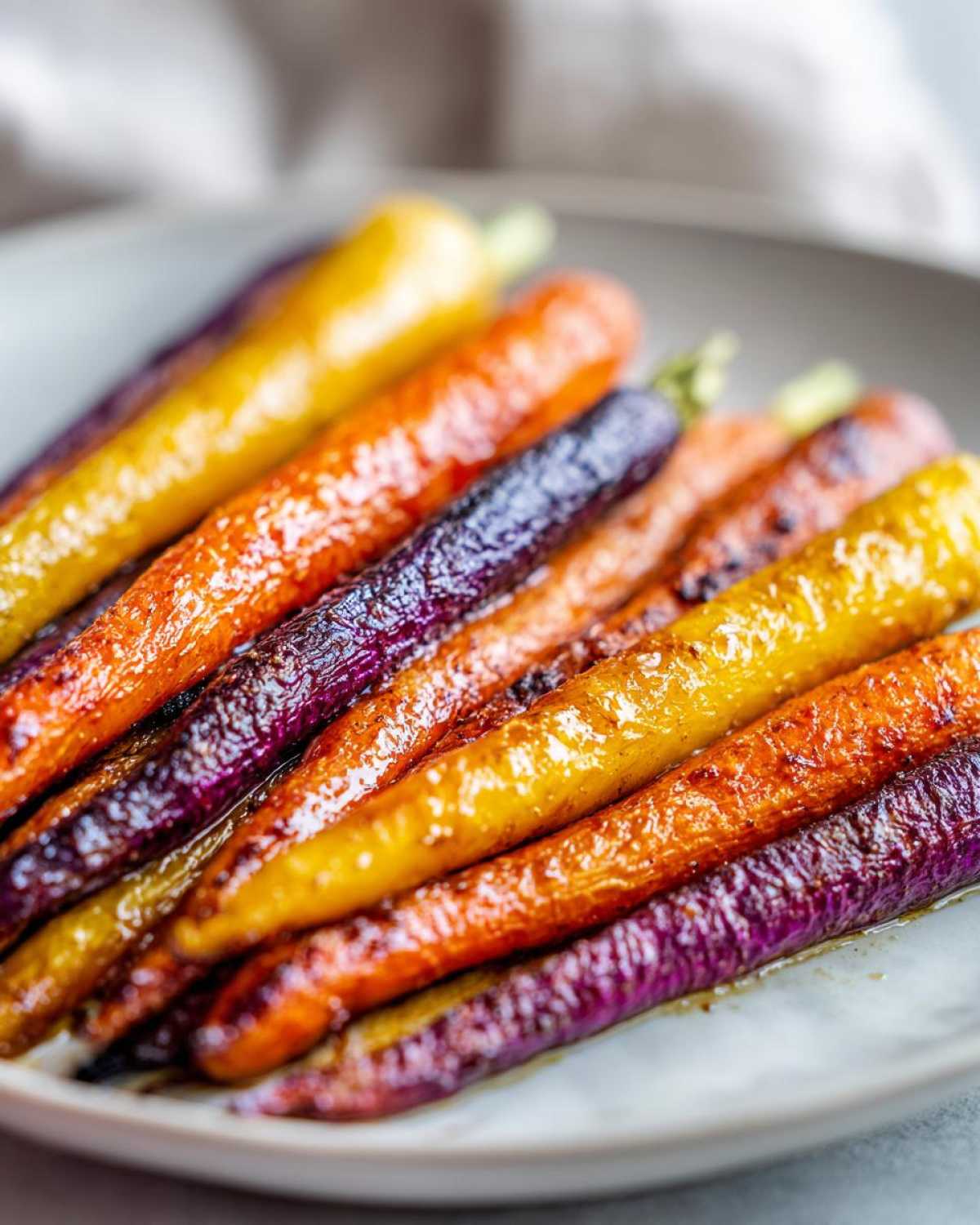Close-up of glossy, caramelized Sheet Pan Roasted Rainbow Carrots with Honey on a light plate.