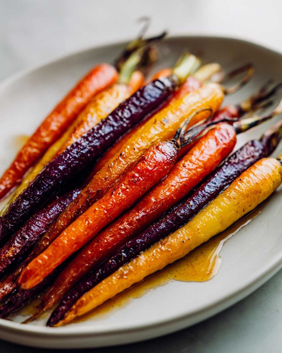Close-up of glossy, roasted Sheet Pan Roasted Rainbow Carrots with Honey on a white platter.